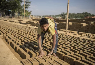 A teenage boy lays bricks out to dry in the sun
