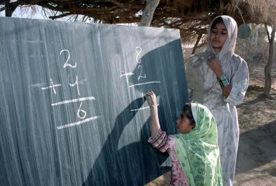 A young girl trying to solve a math with help from her teacher standing next her, Pakistan.