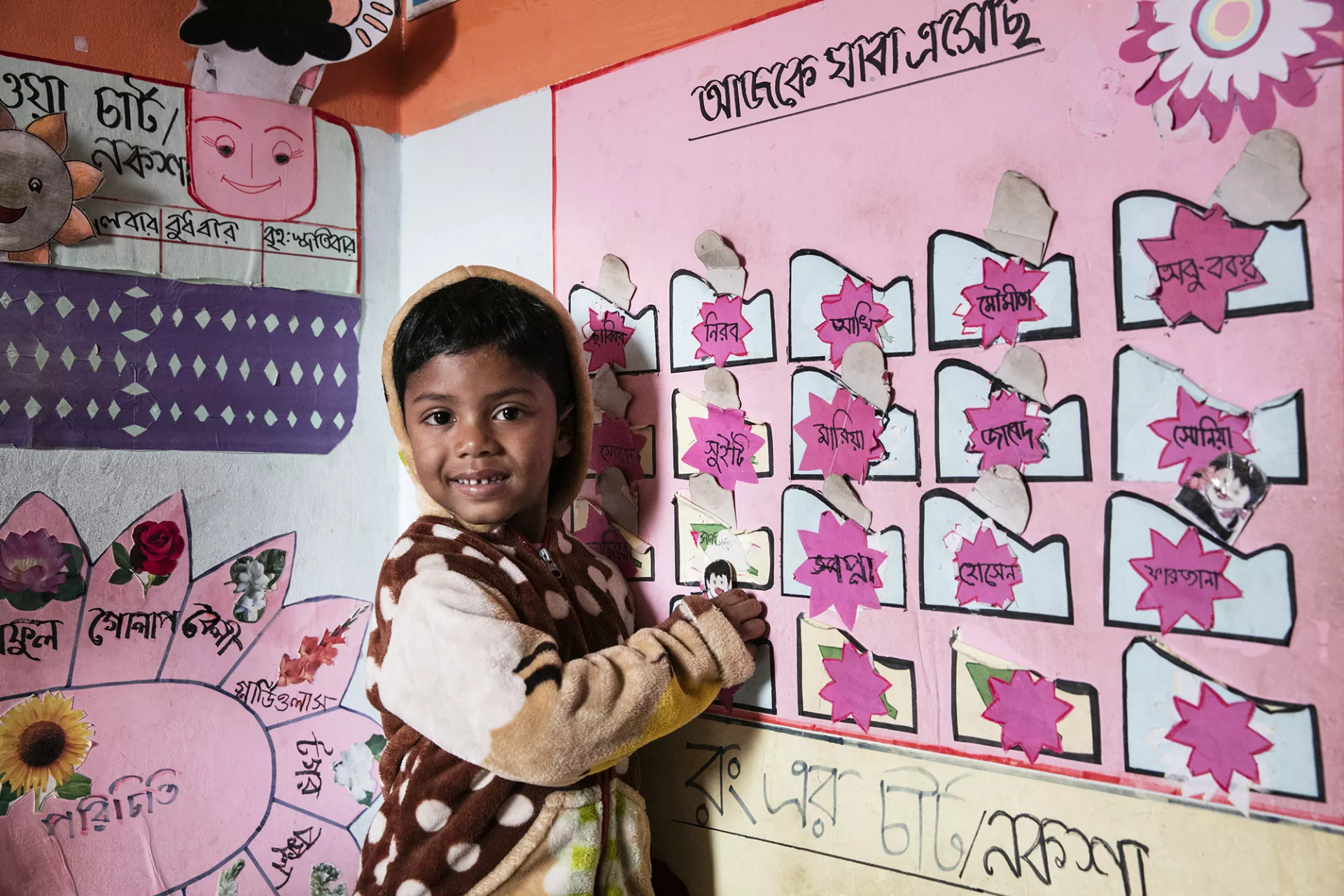 A young child marking off his presence on the color chart at a day care in Bangladesh