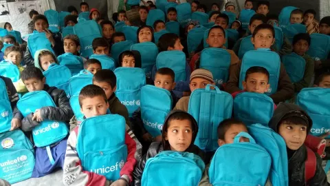 A room full of young students holding blue UNICEF schoolbags